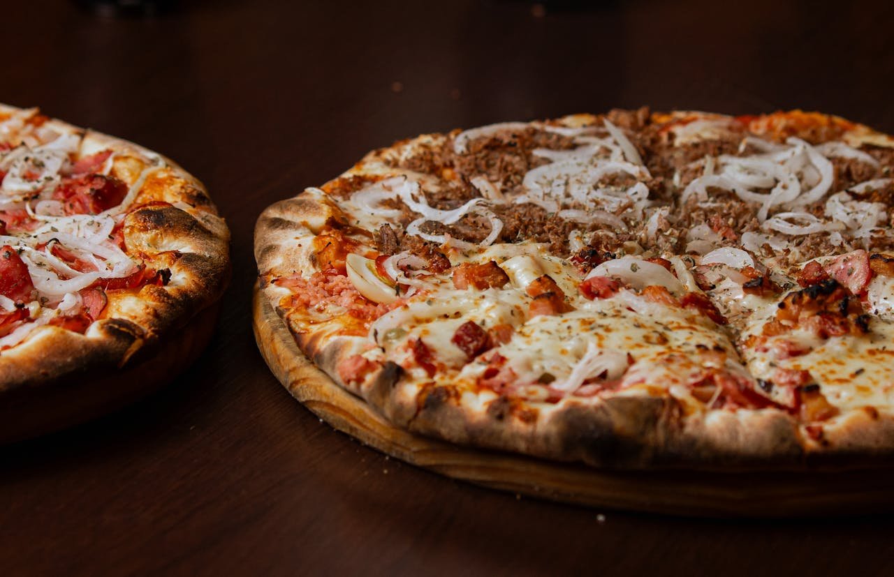 Close-up of two delicious pizzas with pepperoni and onions on a wooden table.